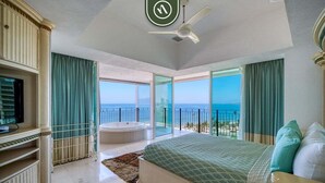 Un dormitorio con una cama grande, televisión, ventilador de techo y vista al océano.