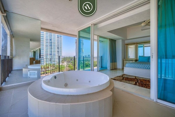 Un intérieur moderne avec une grande baignoire, un balcon offrant une vue sur les immeubles et une porte-fenêtre coulissante donnant sur une chambre.