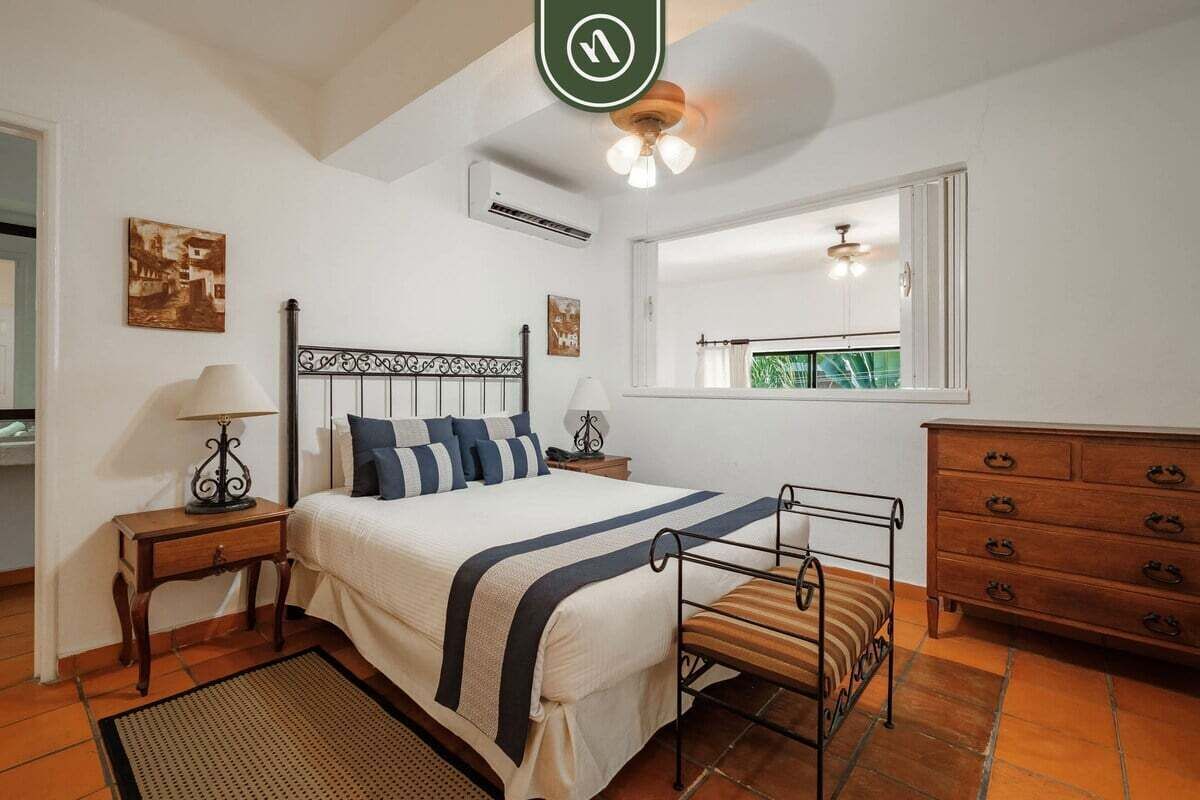 Un dormitorio con cama, mesitas de noche, cómoda, ventana y ventilador de techo.