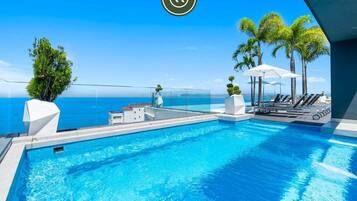 Una piscina infinita moderna con vistas despejadas al océano, rodeada de palmeras y sillones de sol.