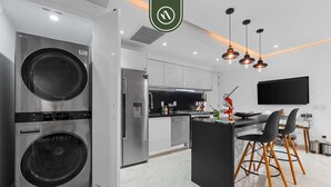 Una cocina moderna con lavadora y secadora integradas, un comedor con televisor y una zona de bar.