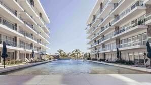 A modern hotel with a central swimming pool, multiple balconies, and sun loungers.