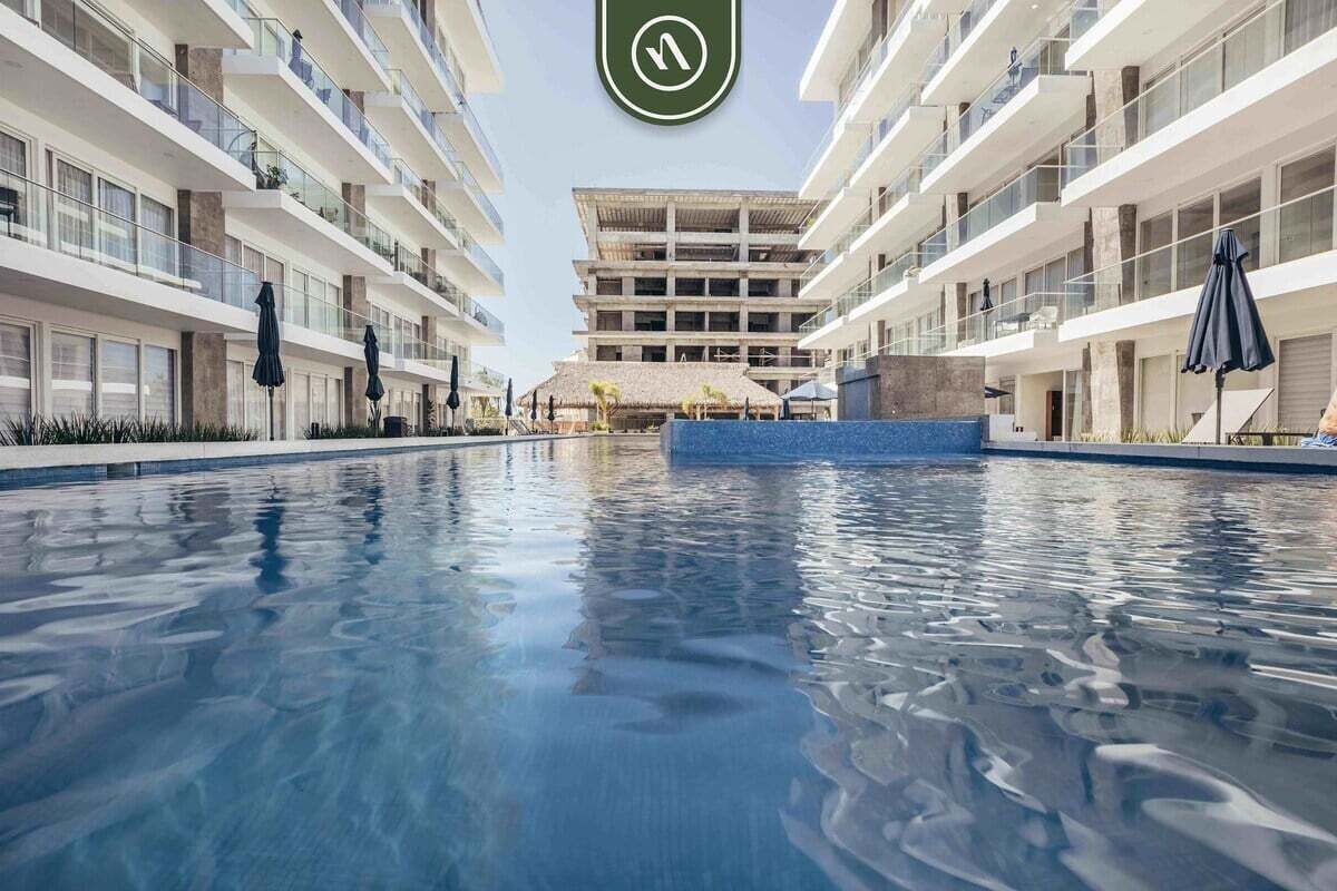 Un hôtel moderne doté d’une piscine centrale, de nombreux balcons et offrant une vue sur un ciel dégagé.