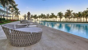 A poolside area with lounge chairs, a decorative wicker chair, and a pool surrounded by palm trees.
