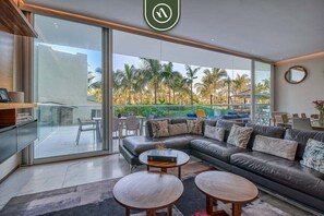 A modern living room with a leather sofa, two round coffee tables, and a large sliding glass door leading to a balcony with palm trees.