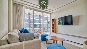 Una habitación de hotel moderna con sofá, reposapiés y un televisor de pantalla plana montado en la pared.