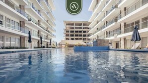 Un hotel moderno con piscina central, varios balcones y diseño arquitectónico tropical.