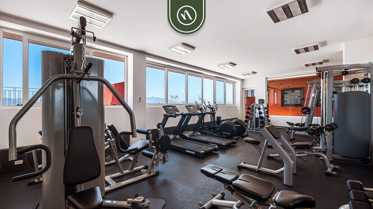 Un gimnasio con diverso equipo de ejercicio, ventanas amplias y vistas al exterior.