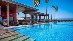 A swimming pool with a covered seating area, palm trees, and a view of the mountains.