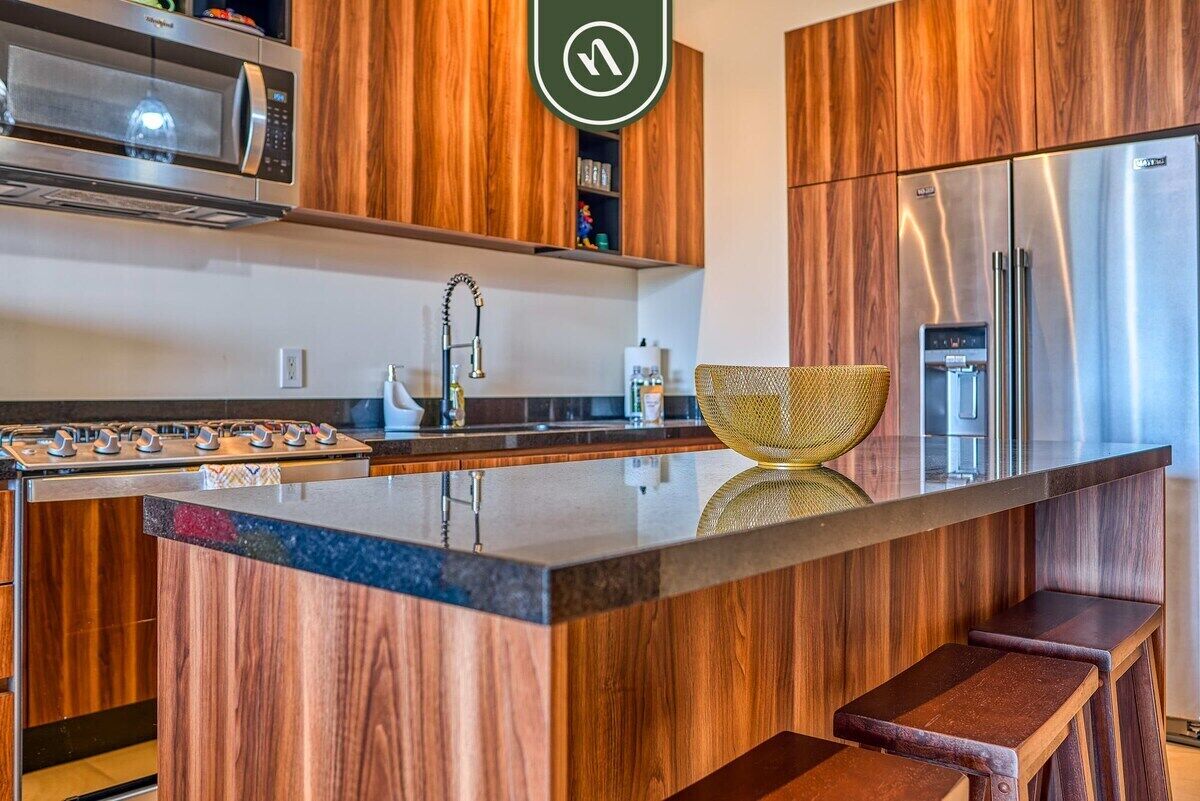 Una cocina moderna con armarios de madera, un refrigerador de acero inoxidable, un microondas y una isla grande con taburetes.