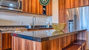 A modern kitchen with wooden cabinets, a stainless steel refrigerator, a microwave, and a large island with stools.