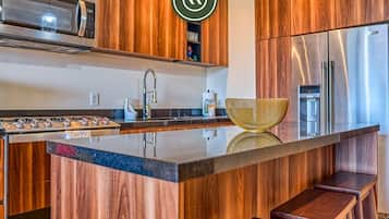Una cocina moderna con armarios de madera, un refrigerador de acero inoxidable, un microondas y una isla grande con taburetes.