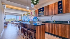 A modern kitchen with wooden cabinets, a central island with stools, and a colorful mural on the wall.