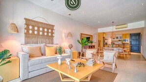 A modern living room with a sofa, coffee table, and decorative items. There is a dining area with chairs and a table. - Amazing 2BR Condo in Nuevo Vallarta - Pool - King (Nuevo Nayarit)