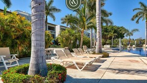 A poolside area with lounge chairs, palm trees, and a building in the background. - Amazing 2BR Condo in Nuevo Vallarta - Pool - King (Nuevo Nayarit)
