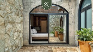 A stone wall, a bed with white linens, a large glass door, and potted plants. - Luxury 3 BR House in Downtown - AC - Peaceful (Oaxaca)