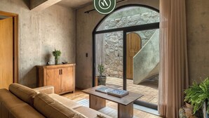 A modern living room with a sofa, a wooden cabinet, a coffee table, and a view through a glass door to an outdoor area. - Luxury 3 BR House in Downtown - AC - Peaceful (Oaxaca)