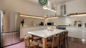 A modern kitchen with a stainless steel refrigerator, a marble island, wooden chairs, and pendant lighting. - Centric 3BR Condo in Downtown in Oaxaca (Oaxaca)
