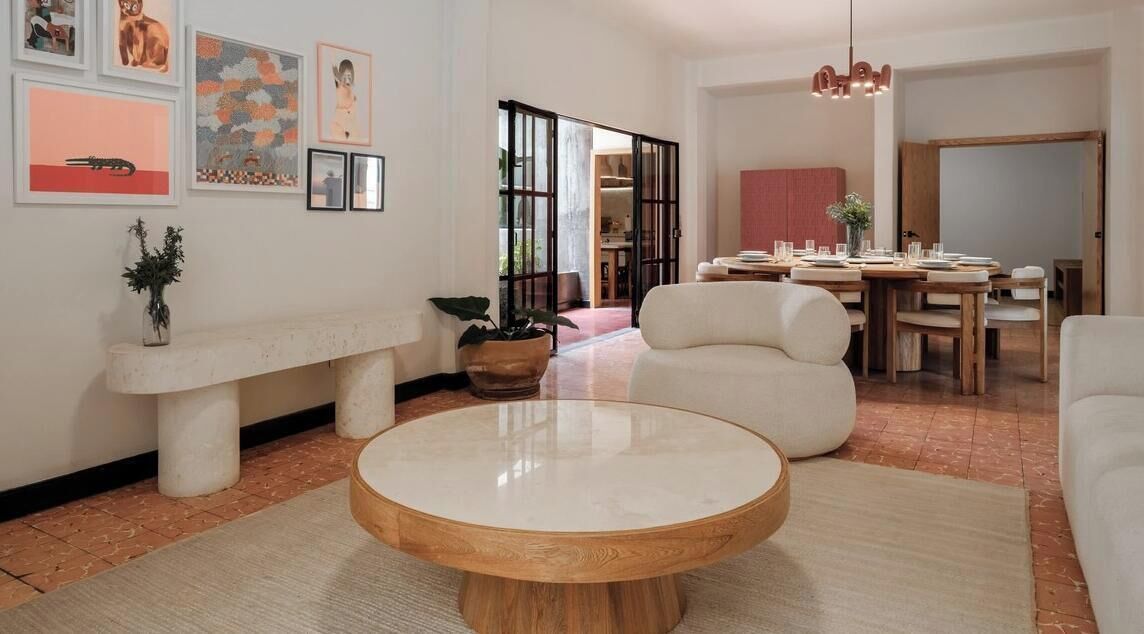 A modern living room with a round coffee table, a bench, and a dining area with a table and chairs.