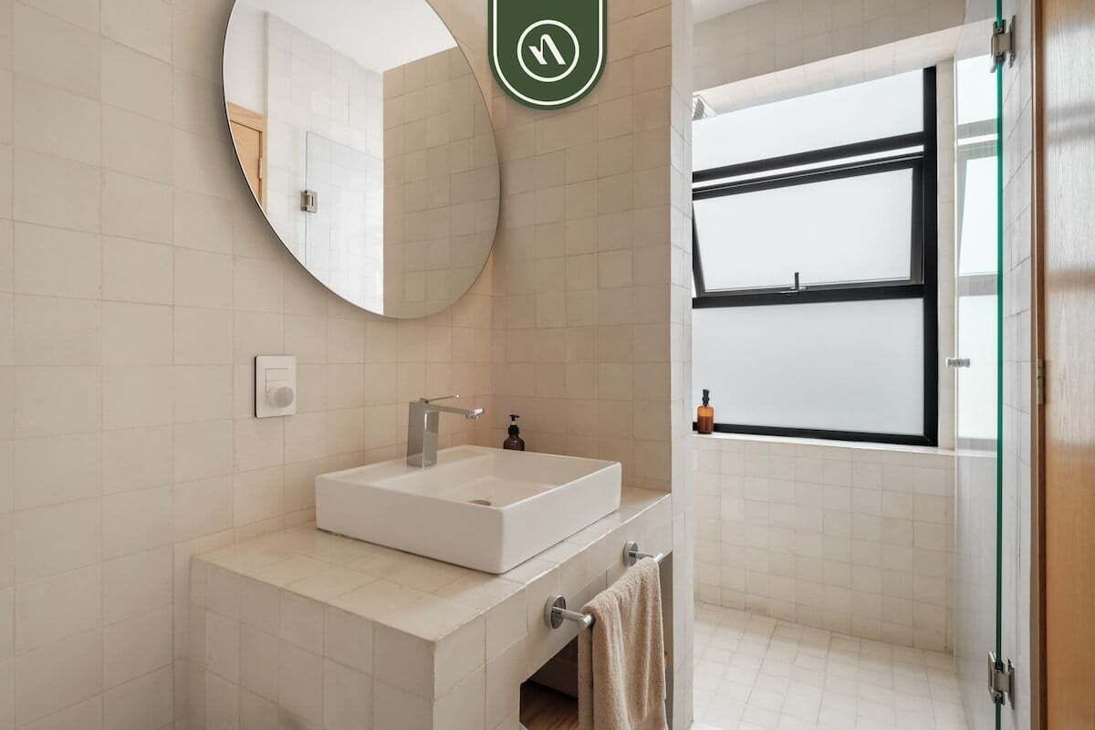 A modern bathroom with a large mirror, a white sink, and a towel rack.