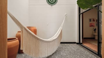 A hammock in a hallway with terracotta pots and a large plant.