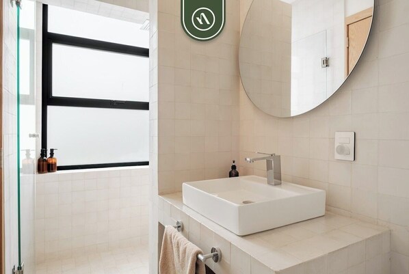 Een moderne badkamer met een groot raam, een witte wastafel, een ronde spiegel en een handdoekhouder.