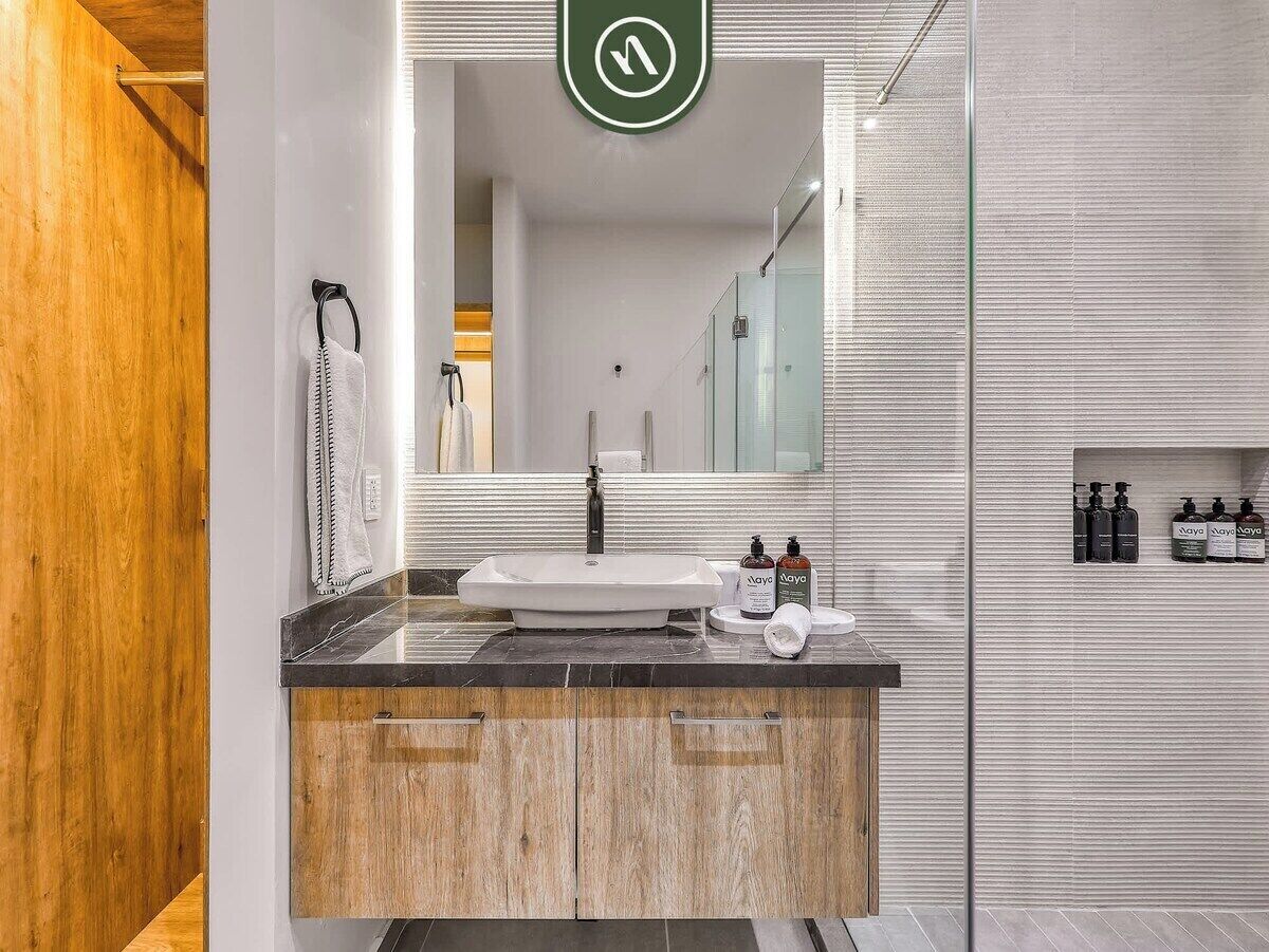 A modern bathroom with a large mirror, a sink, wooden cabinets, and a glass shower enclosure.