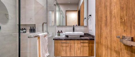 A modern bathroom with a glass shower enclosure, a wooden vanity with a sink, and a towel rack.