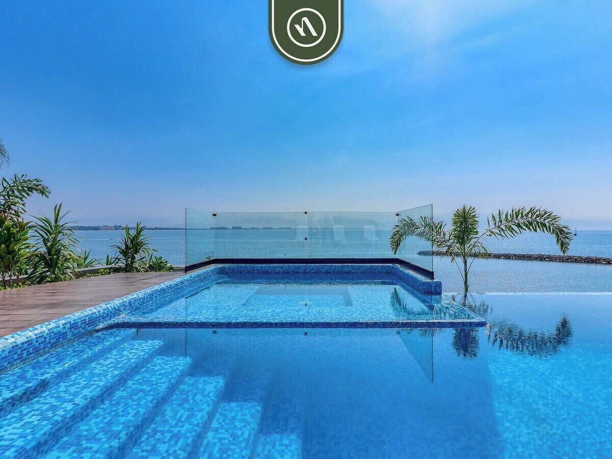 Una piscina infinita de color azul claro con vistas al mar y a la costa lejana.