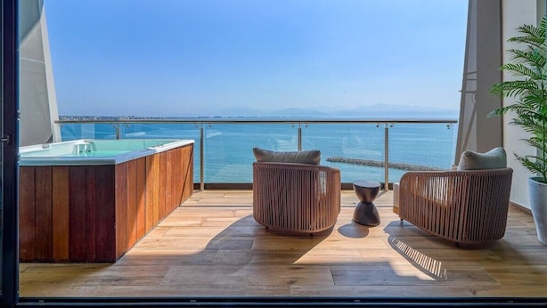A balcony with a wooden floor, two wicker chairs, a small table, and a hot tub. - Luxury Oceanfront 3 BR Condo With Balcony (La Cruz de Huanacaxtle)