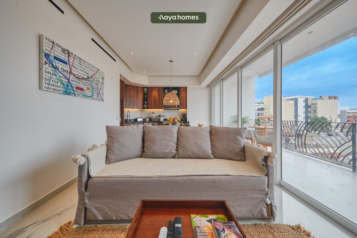 Un salon moderne avec un canapé, une table basse et une vue sur la ville grâce à de grandes fenêtres.
