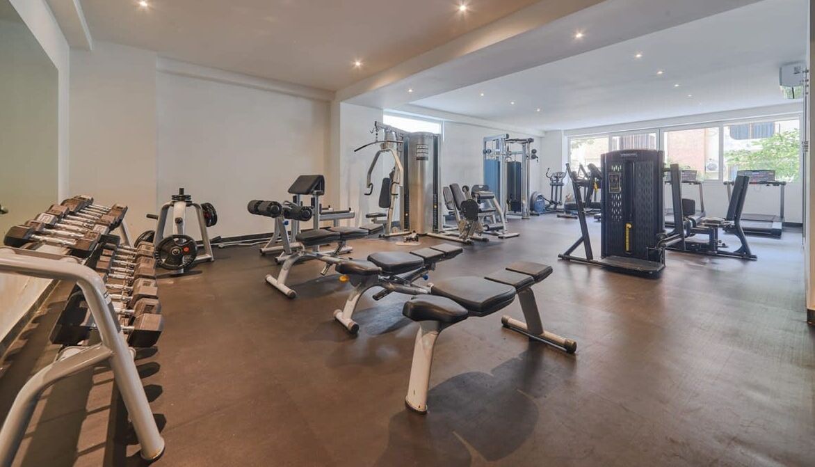 Ein geräumiges Fitnessstudio mit verschiedenen Trainingsgeräten, darunter Hanteln, Bänke und Kraftgeräte.