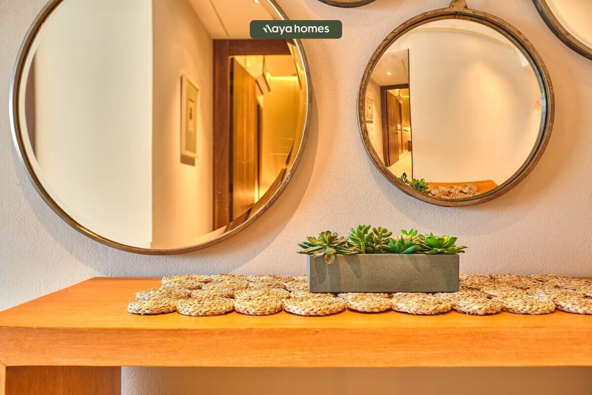 Un pasillo con dos espejos redondos en la pared, una mesa de madera con una pequeña planta y individuales tejidos, y un letrero que dice 'Aya homes'.