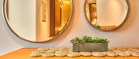 Un pasillo con dos espejos redondos en la pared, una mesa de madera con una pequeña planta y individuales tejidos, y un letrero que dice 'Aya homes'.