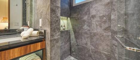 A modern bathroom with a marble shower, a vanity with a mirror, and a towel rack.