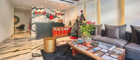 A modern hotel lobby with a reception desk, a sofa, a coffee table with magazines, and a decorative Christmas tree.