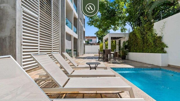 Ein Poolbereich mit Liegestühlen und einem Tisch, umgeben von einer weißen Mauer und Pflanzen.