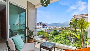 Ein Balkon mit einer Couch, einem Glastisch und Blick auf eine Stadtlandschaft mit Bergen im Hintergrund.