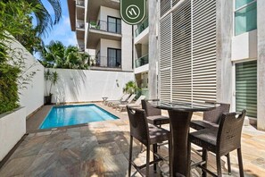 A modern building with a swimming pool, outdoor seating, and a balcony with plants. - Amazing 1BR Condo - Pool - BBQ in Versalles (Puerto Vallarta)