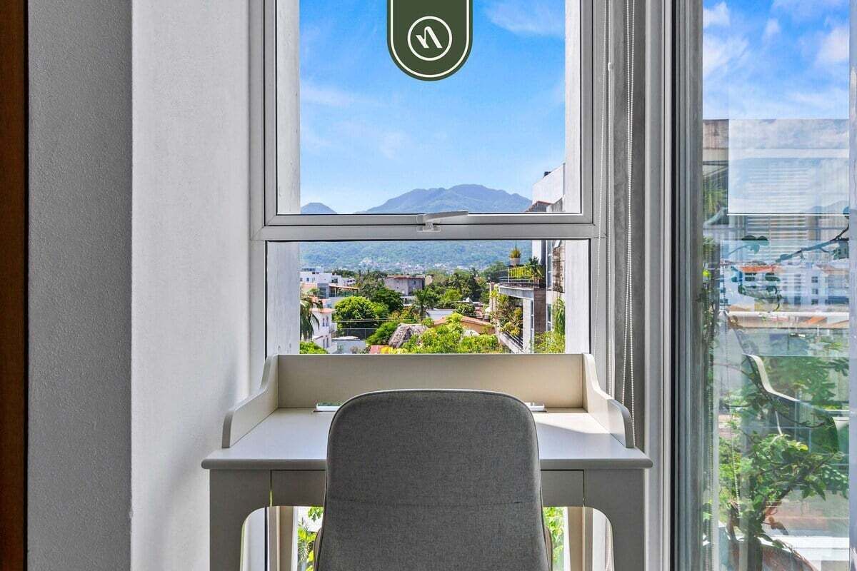 Et vindue med udsigt over bybilledet, et skrivebord og en stol.
