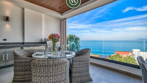 Un balcón con mobiliario de mimbre, una mesa de vidrio y vista al mar.