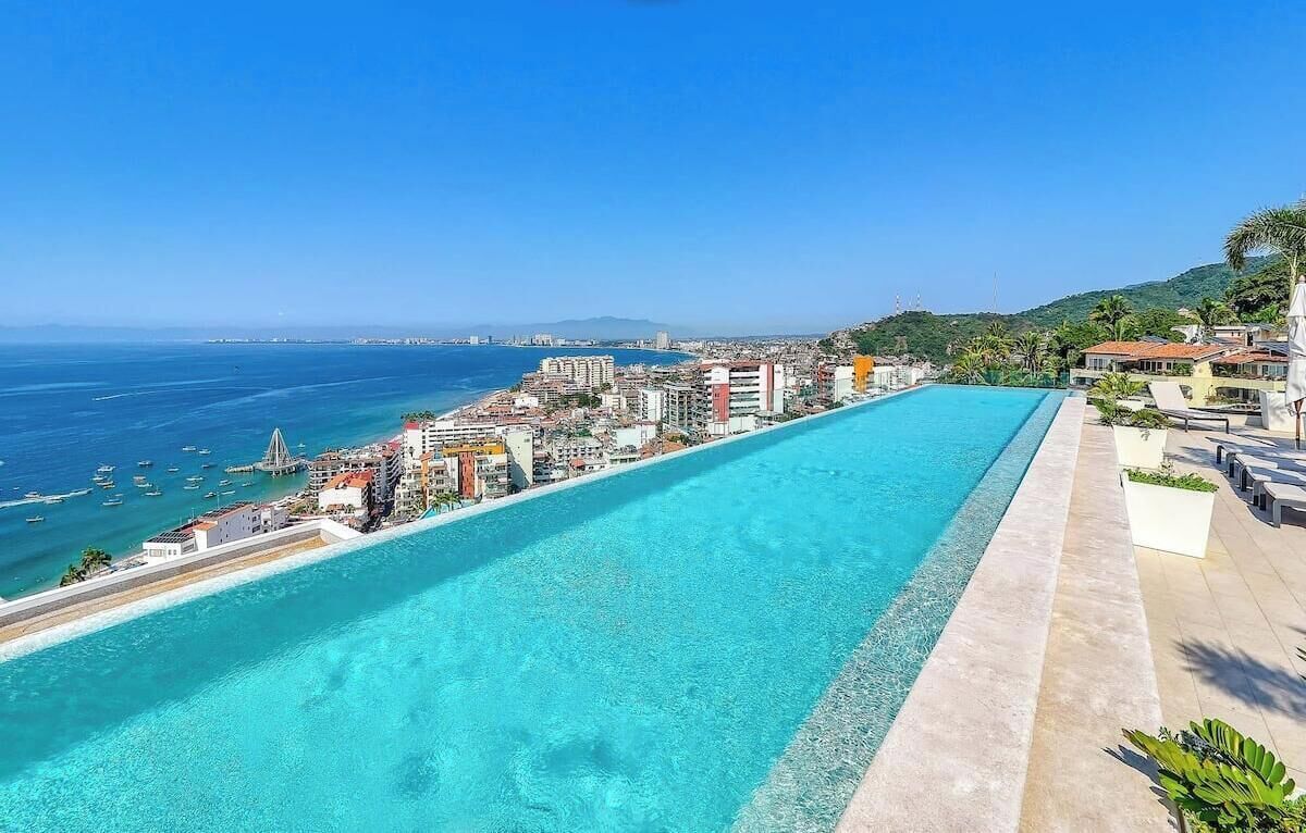 A long swimming pool with a clear view of the ocean and cityscape.