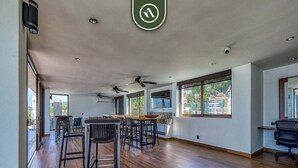 Una habitación amplia con suelo de madera, ventiladores de techo y grandes ventanas que ofrecen vistas al exterior.