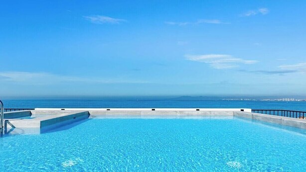 A clear blue swimming pool with a view of the ocean and distant cityscape. - Brand New 1 BR Condo Right Next to the Malecon (Puerto Vallarta)