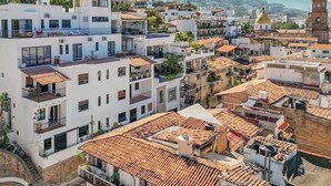 A multi-story building with balconies, a rooftop terrace, and a view of the surrounding cityscape. - Brand New 1 BR Condo Right Next to the Malecon (Puerto Vallarta)