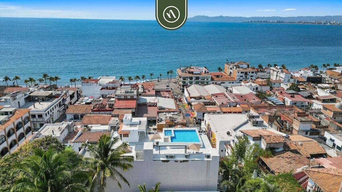 Un pueblo costero con zona de piscina, edificios con techos de tejas rojas y palmeras.