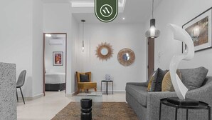 A modern living room with a grey sofa, a coffee table, a rug, and a wall-mounted mirror. - Brand New 1 BR Condo Right Next to the Malecon (Puerto Vallarta)