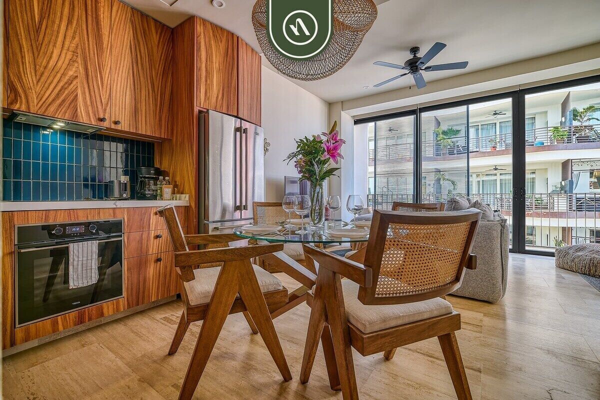 A modern kitchen with wooden cabinetry, a glass dining table, and a view of a residential building.