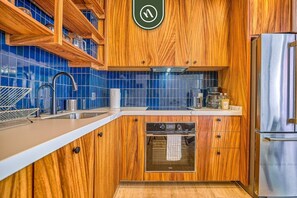A kitchen with wooden cabinets, a stainless steel refrigerator, a dishwasher, and a blue tiled backsplash.