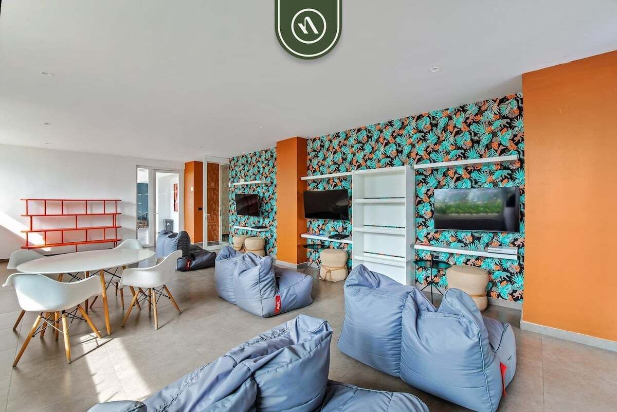 A modern living room with a white table, blue bean bags, a TV on the wall, and a patterned wallpaper.